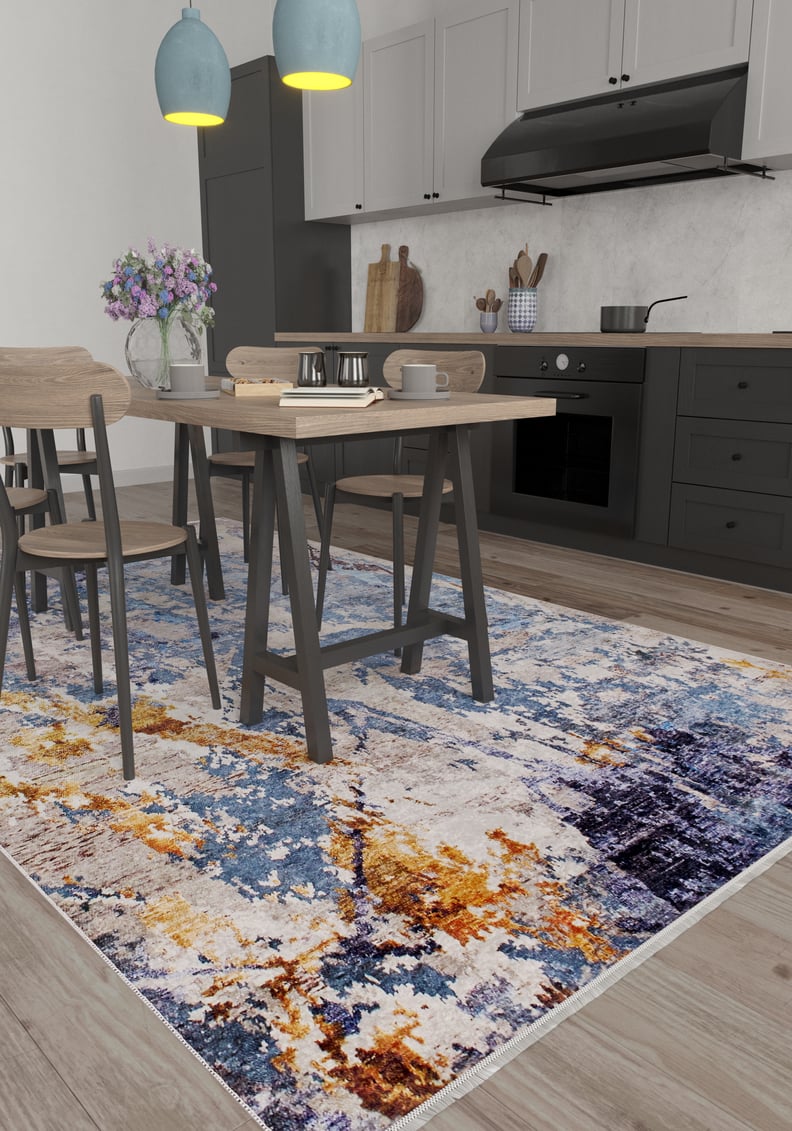A modern kitchen with light wood floors, black lower cabinets, and a dining table for four features the Enigmatic Elegance - Washable Rug - JR787 in blue, paired with two blue pendants and a vase of flowers—a vibrant, practical choice for high-traffic areas.