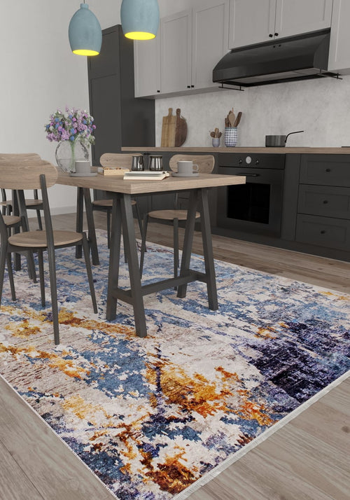 Load image 1 in gallery view. A modern kitchen and dining area with light wood furniture, gray cabinets, and a stovetop. The Enigmatic Elegance - Washable Rug - JR787 (Custom Size) in vibrant blue, orange, and yellow covers the floor—ideal for high-traffic areas. A vase with purple flowers sits on the table.