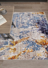 The Enigmatic Elegance - Washable Rug - JR787 (Custom Size), featuring vibrant blue, yellow, and white patterns, is placed on a light wood floor near a wooden table with an open book and coffee—ideal for high-traffic areas.