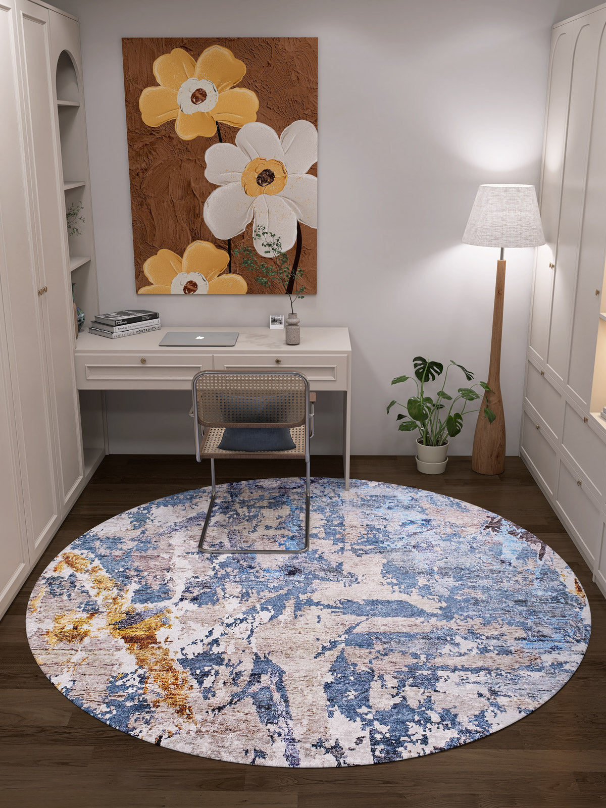 A cozy home office features a white desk, chair, and the Enigmatic Elegance - Washable Rug - JR787 (Custom Size)—ideal for high-traffic areas. Nearby are a floor lamp, a large floral painting with white and yellow blooms, and a small potted plant beside the desk.