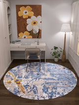 A cozy home office features a white desk, chair, and the Enigmatic Elegance - Washable Rug - JR787 (Custom Size)—ideal for high-traffic areas. Nearby are a floor lamp, a large floral painting with white and yellow blooms, and a small potted plant beside the desk.