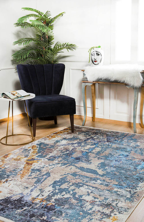 Load image 1 in gallery view. A modern living space features a dark velvet chair, small round table, potted plant, white-furred bench with a face vase, and the Enigmatic Elegance - Washable Rug - JR787 (Custom Size), ideal for high-traffic areas.