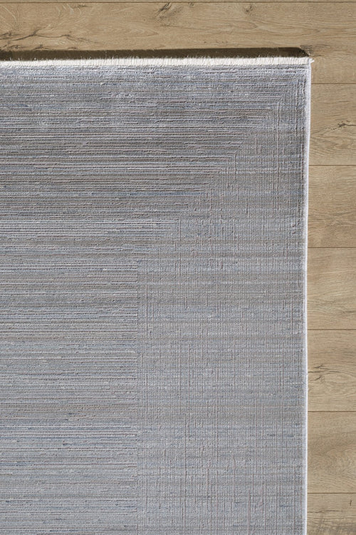 Load image 1 in gallery view. A close-up of the Essential Weave Modern Grey Rug - EW2836 (Outlet) US on a wooden floor, showing its light gray color, subtle linear design, and neatly finished edges.