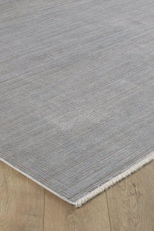 Load image 1 in gallery view. A close-up of the Essential Weave Modern Grey Rug - EW2836 (Outlet) US, a rectangular machine-made rug in a neutral grey with subtle textured patterns and short fringes, displayed on a natural-finish wooden floor with visible grain.