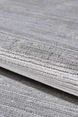 A close-up of the Essential Weave Modern Grey Rug - EW2836 (Outlet) US, machine-made with grey and beige horizontal linear patterns, shown rolled on a matching carpeted floor.