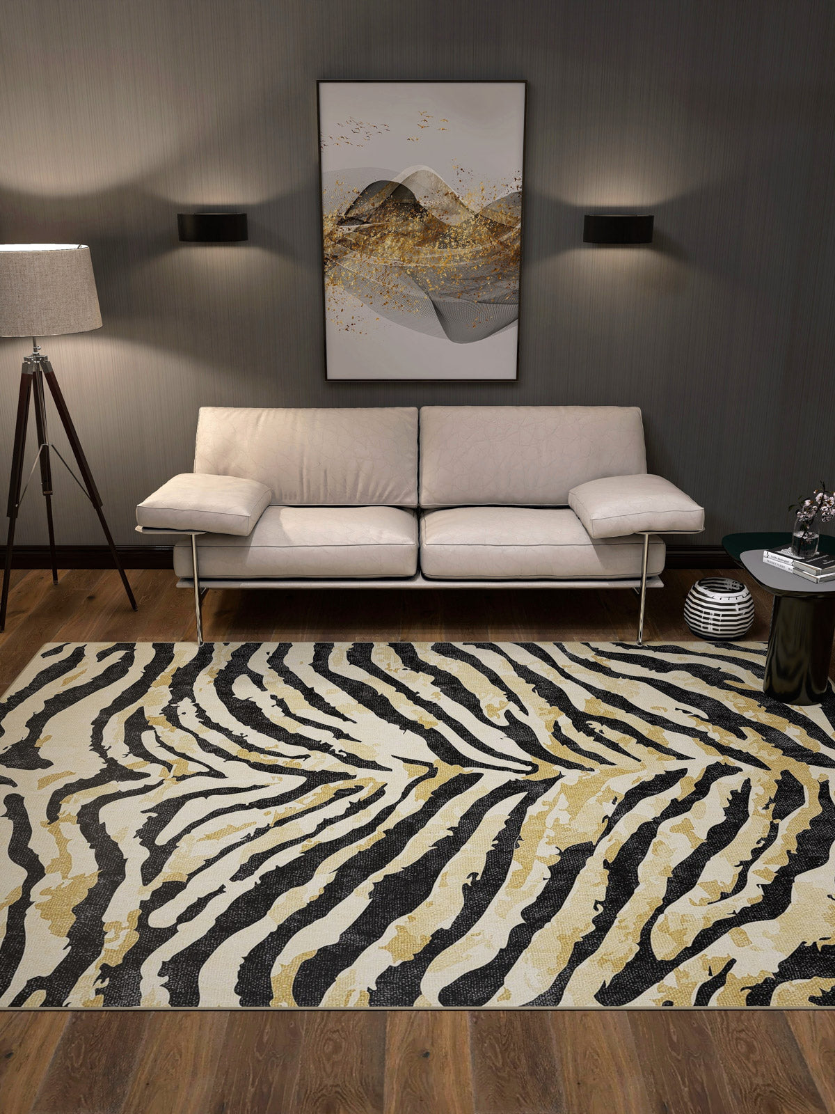 A modern living room features a white sofa, the Eternal Weave - Washable Rug - JRN39 in a zebra black, white, and gold pattern for high-traffic areas, a tripod floor lamp, abstract wall art, dark walls, and wooden flooring.