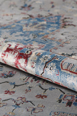 A close-up shows the rolled corner of the Ethereal Garden Medallion Rug - Grey - 2222C, featuring abstract red, blue, and beige designs on a soft gray background. The textured weave and detail of this grey and blue rug are clearly visible.