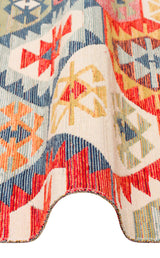 A close-up of the Ethnic Mix - Kilim - NMD01 rug displays its multicolour geometric patterns in red, blue, yellow, and cream, with a wavy edge that accentuates the texture and intricate designs.