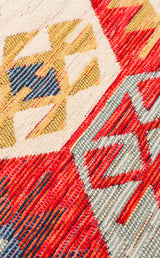Close-up of the "Ethnic Mix - Kilim - NMD01" rug, featuring multicolour geometric patterns and tribal motifs in red, yellow, blue, and cream with visible texture and intricate stitching.