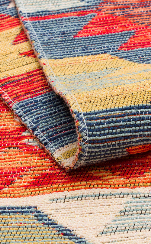 Load image 1 in gallery view. A close-up of the Ethnic Mix - Kilim - NMD01 rug reveals vibrant geometric patterns in red, yellow, blue, and cream. The slightly folded edge highlights textured fabric and tribal motifs stitched along the border.
