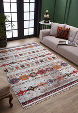 The Ethno Expanse - Machine-Washable Rug - JR5046 (Custom Size) adds color and texture to a living room with a gray sofa, brown chair, round side table, and green paneled walls on a wooden floor near tall windows.