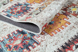 A close-up of the Ethno Expanse - Machine-Washable Rug - JR5046 (Custom Size) shows its colorful geometric pattern in red, blue, yellow, and orange, with one corner flipped to reveal the textured underside.