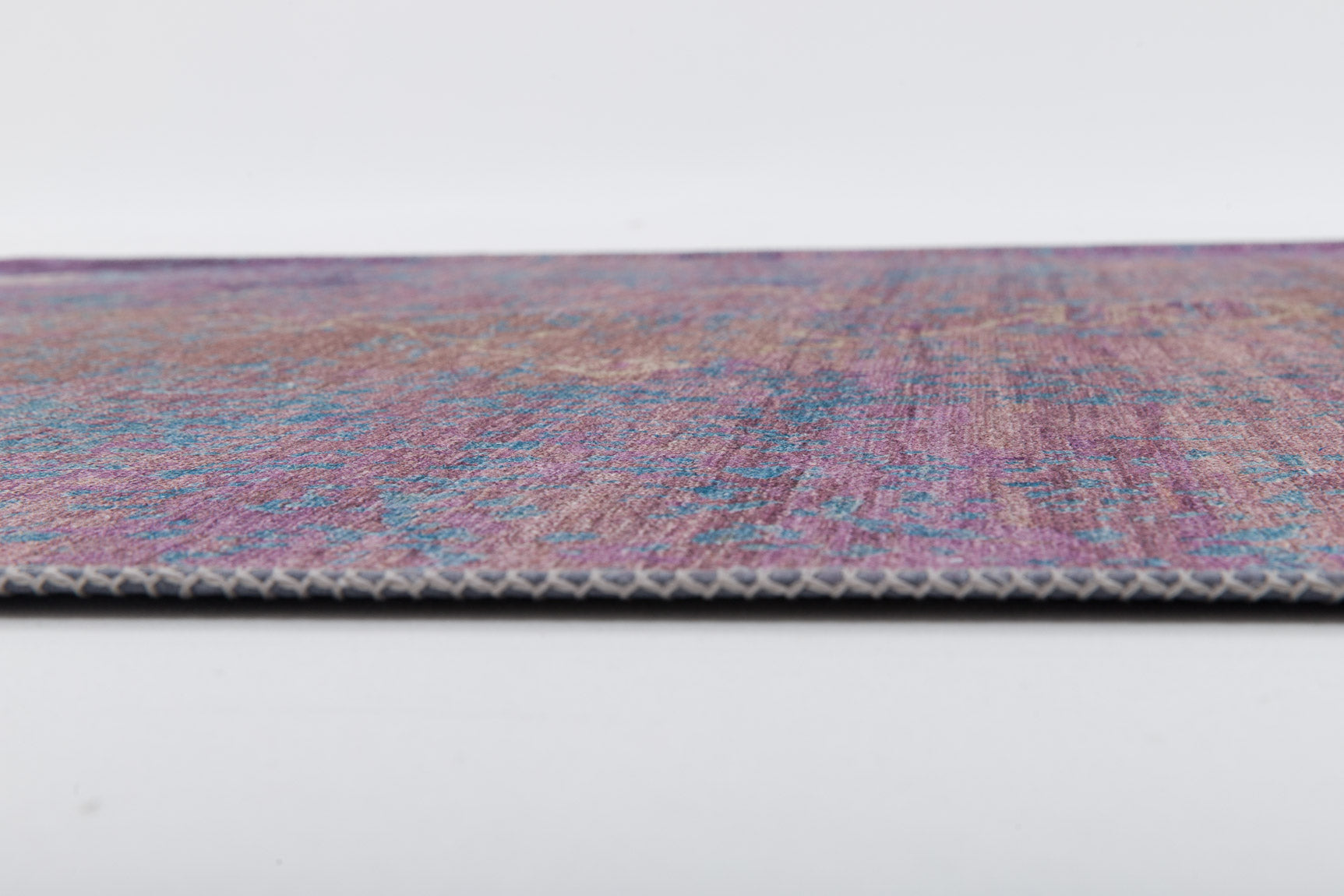 A close-up, side view of the Faerie Weave - Washable Rug - JRS005, featuring a thin design with a vibrant purple and blue pattern against a white background—perfect for high-traffic areas.