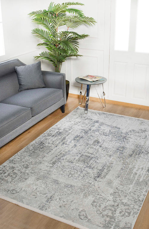 Load image 1 in gallery view. A modern living room with a gray sofa, throw pillow, round glass side table with magazines, tall green potted plant, and the Faint Memories - Washable Rug - JR1437 (Custom Size) in gray-anthracite on a wooden floor.