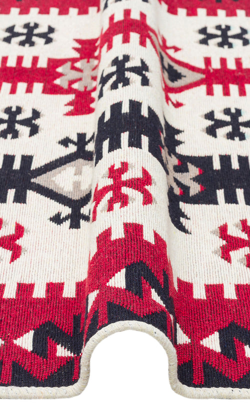 Load image 1 in gallery view. A close-up of the Flame Line - Washable Reversible Kilims - AR32, showing a bold red, black, and cream geometric pattern with a folded edge featuring zigzag and star motifs.