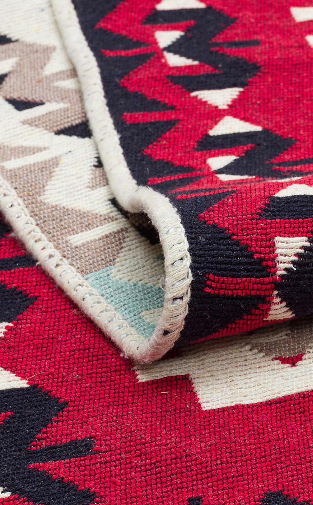 A close-up of the Flame Line - Washable Reversible Kilims - AR32 shows red, black, white, and beige tribal geometric patterns with a folded edge and detailed border stitching, highlighting its intricate craftsmanship.