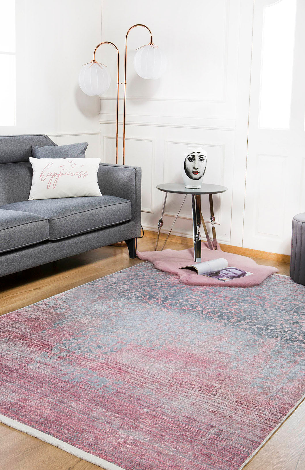 A modern living room with a gray sofa, a “happiness” pillow, and the Floral Filigree - Washable Rug - JR341 (Custom Size)—perfect for high-traffic areas—plus a small round table, decorative face vase, globe floor lamp, and magazine on the rug.