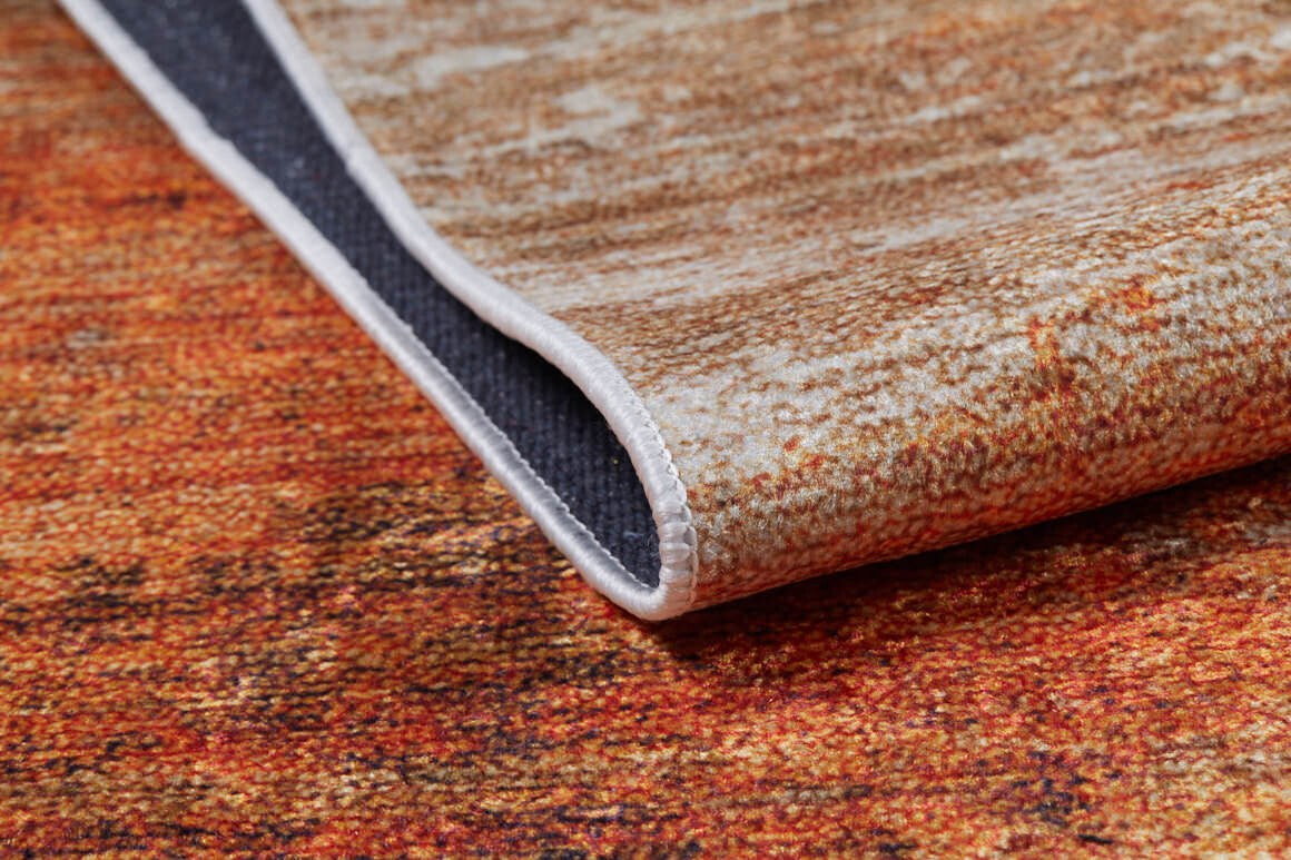 A close-up of the Fluffy Brushed - Washable Rug - JR584 (Custom Size) in orange with warm brown tones, showing a folded corner that reveals its dark textured underside and neat stitching—perfect for high-traffic areas.