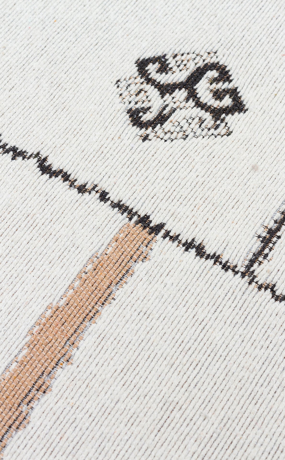 A close-up of the Fog Detail - Washable Double-Sided Kilims - AR40 shows its reversible, recycled cotton design with black and tan geometric lines on a cream background, highlighting visible fabric texture and detailed stitching.