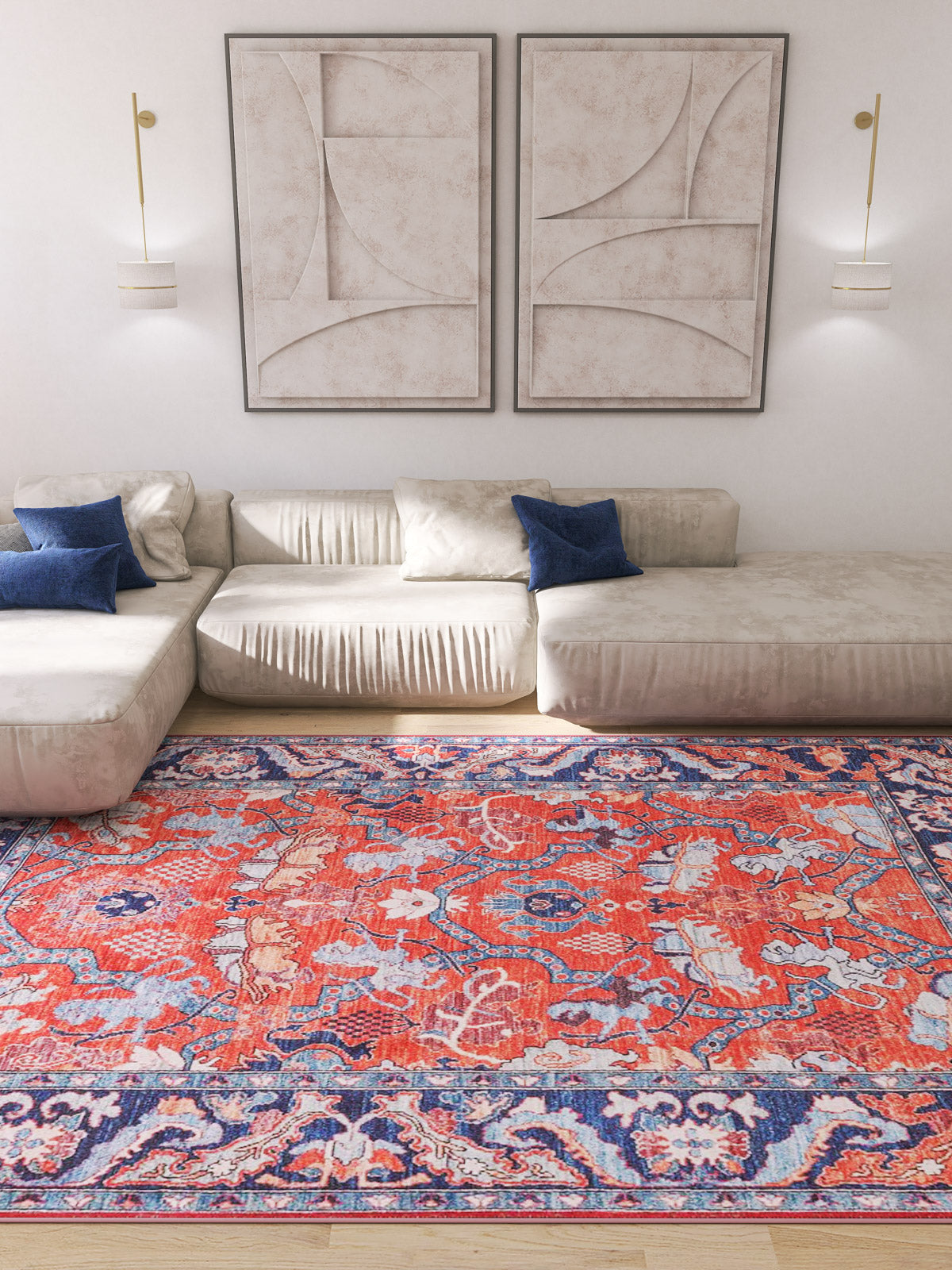 A modern living room with cream sofas, blue accent pillows, abstract art, and the Galea Turkish-Design Coral Washable Rug (LCC3027)—ideal for high-traffic areas—adds vibrant red and blue patterns to a light wood floor.