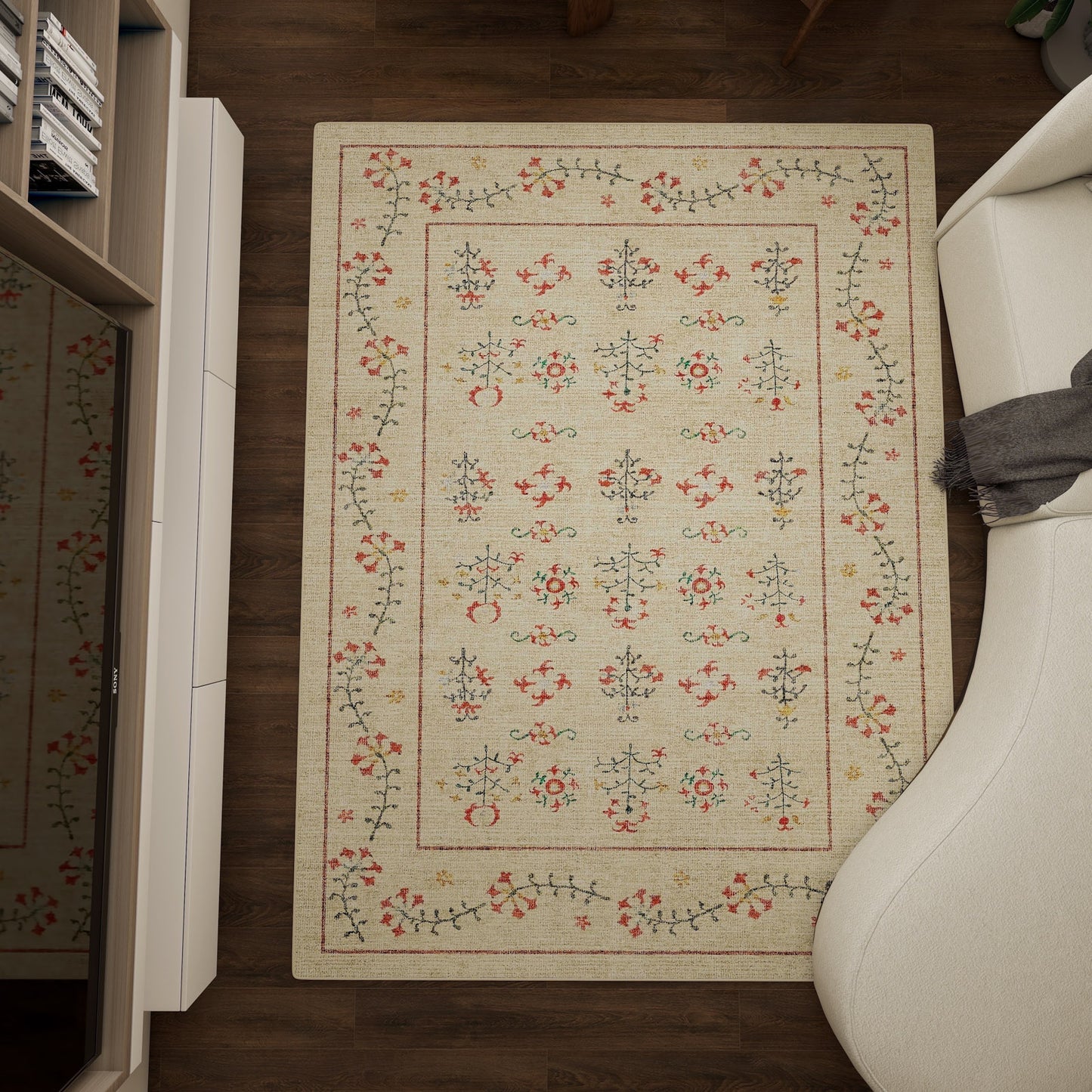 The Garden Cream - Washable Rug - JRN1026 (Custom Size), a rectangular beige rug with a red, green, and blue floral pattern, lies between a white sofa and shelves on a dark wood floor; a gray blanket rests on the sofa’s armrest.