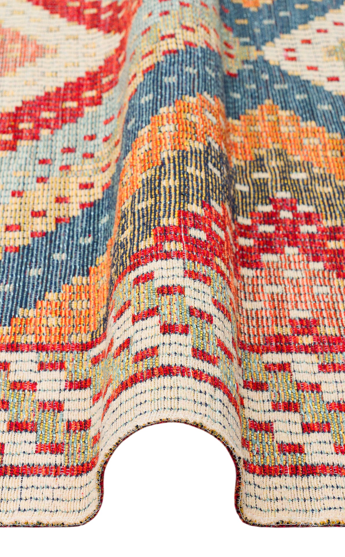 A close-up of the Garnet Print - Kilim - NMD10 rug showcases its blue, orange, yellow, and cream geometric tribal patterns. Partially folded to reveal texture and thickness, this low-pile polyester rug offers richness and lasting durability.