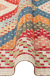 A close-up of the Garnet Print - Kilim - NMD10 rug showcases its blue, orange, yellow, and cream geometric tribal patterns. Partially folded to reveal texture and thickness, this low-pile polyester rug offers richness and lasting durability.