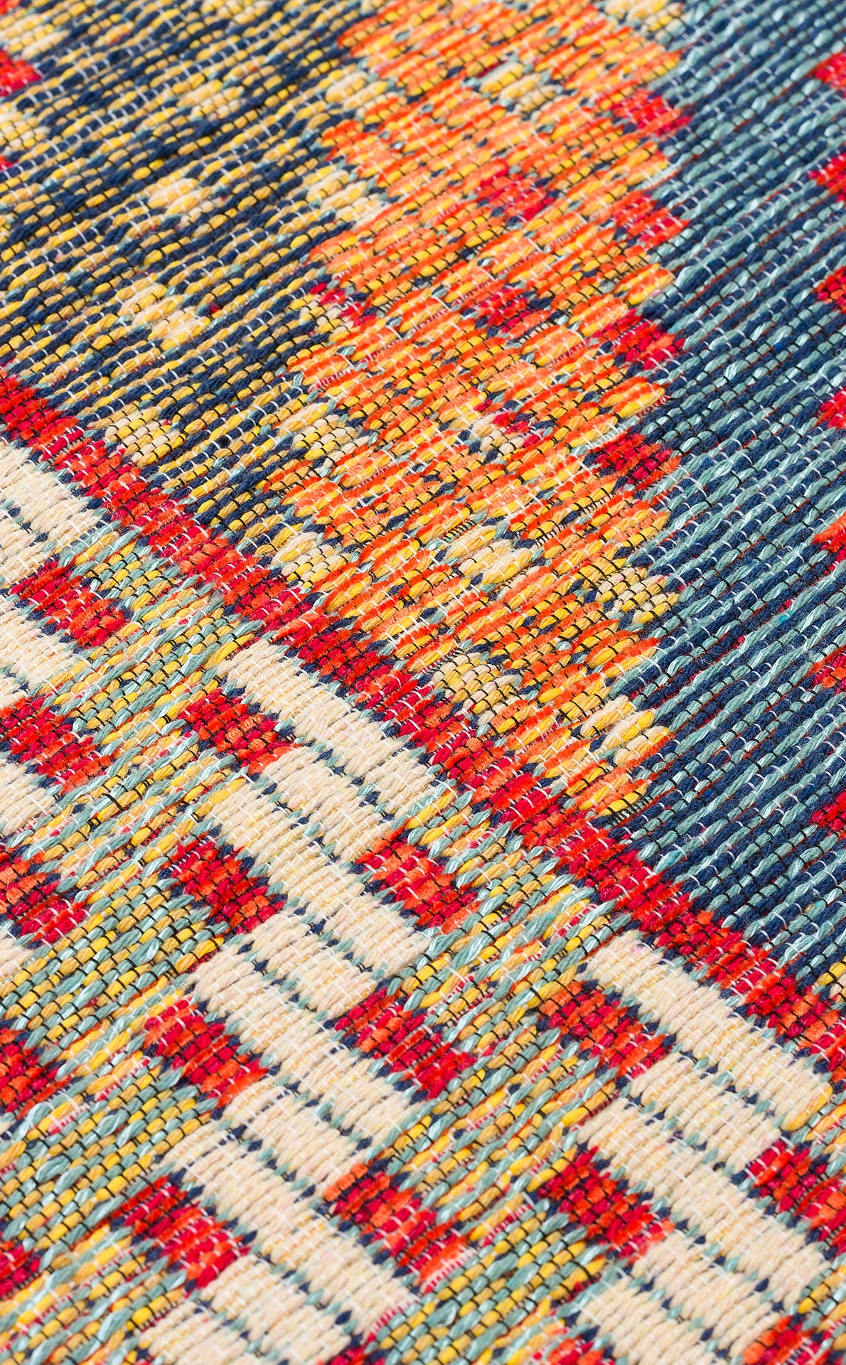 Close-up of the Garnet Print - Kilim - NMD10 rug, showcasing its vibrant geometric patterns in red, orange, blue, and cream. The detailed low-pile polyester weave highlights a textured and intricate tribal-inspired design.