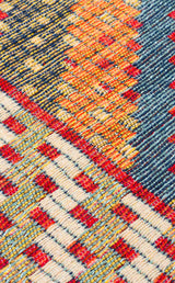 Close-up of the Garnet Print - Kilim - NMD10 rug, showcasing its vibrant geometric patterns in red, orange, blue, and cream. The detailed low-pile polyester weave highlights a textured and intricate tribal-inspired design.