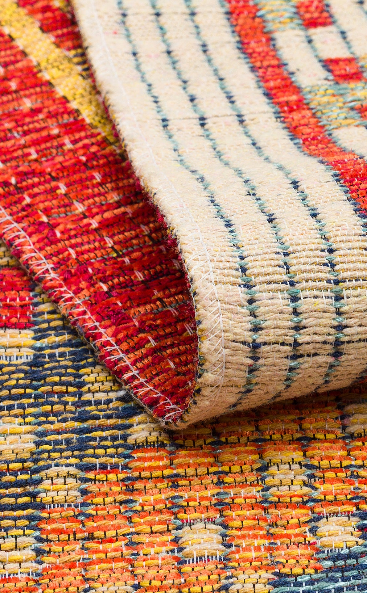 A close-up of the Garnet Print - Kilim - NMD10 rug, low-pile polyester with red, yellow, blue, and cream tribal geometric patterns. The front and back show visible texture and stitching on this stylish rug.