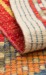 A close-up of the Garnet Print - Kilim - NMD10 rug, low-pile polyester with red, yellow, blue, and cream tribal geometric patterns. The front and back show visible texture and stitching on this stylish rug.