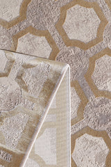 A close-up of the Geometric Down Mid Century Modern Rug - M534B, showcasing its beige, taupe, and gold lattice pattern. One corner is folded to display the rug’s machine-made underside and detailed edge stitching.