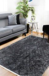 A modern living room with a gray sofa, black chair, Geometric Gems - Washable Rug - JR1342 (Custom Size) in black and gray—ideal for high-traffic areas—round white side table, decorative vase, green potted plant, and light wooden flooring.