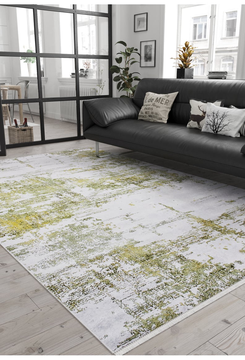 A modern living room features a black leather sofa, decorative pillows, a potted plant, and the Geometric Geometry - Washable Rug - JR1290 (Custom Size), showcasing white abstract patterns—ideal for high-traffic areas with abundant natural light.