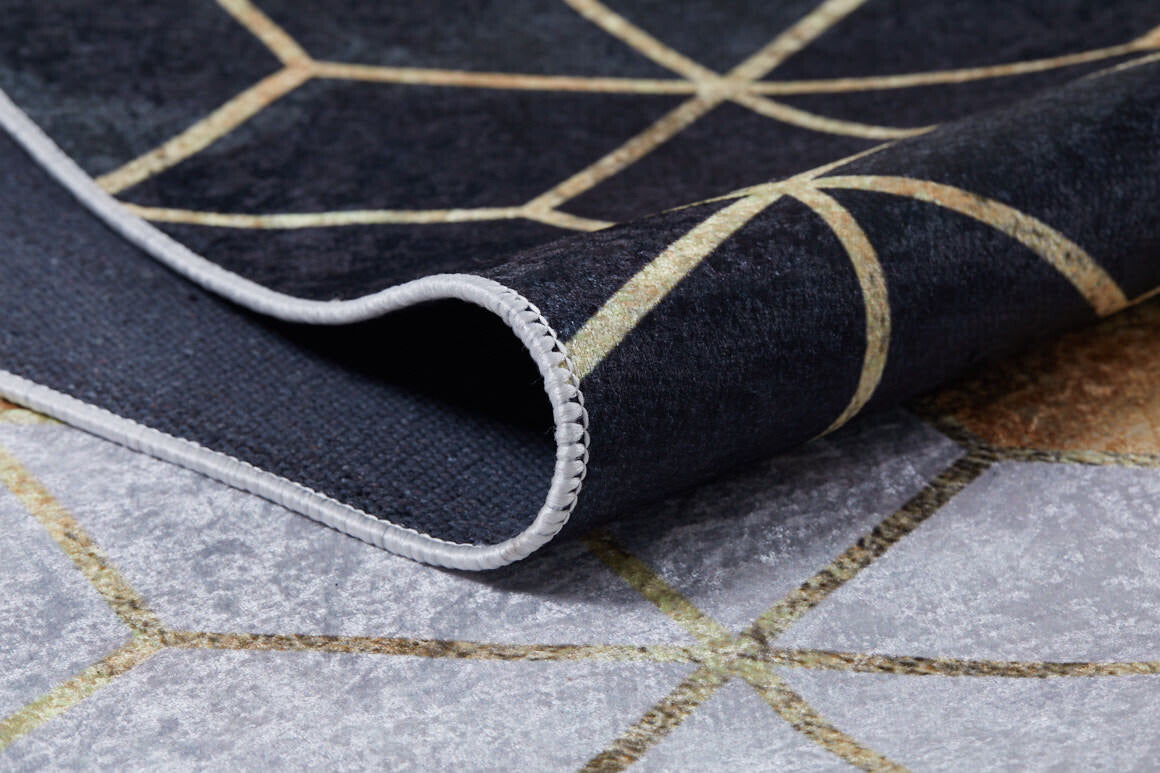 A close-up of the Geometric Harmony - Washable Rug - JR1271 (Custom Size) shows its modern black, gray, and gold geometric pattern. One corner is folded to display the textured edge and underside, highlighting its washable design for high-traffic areas.