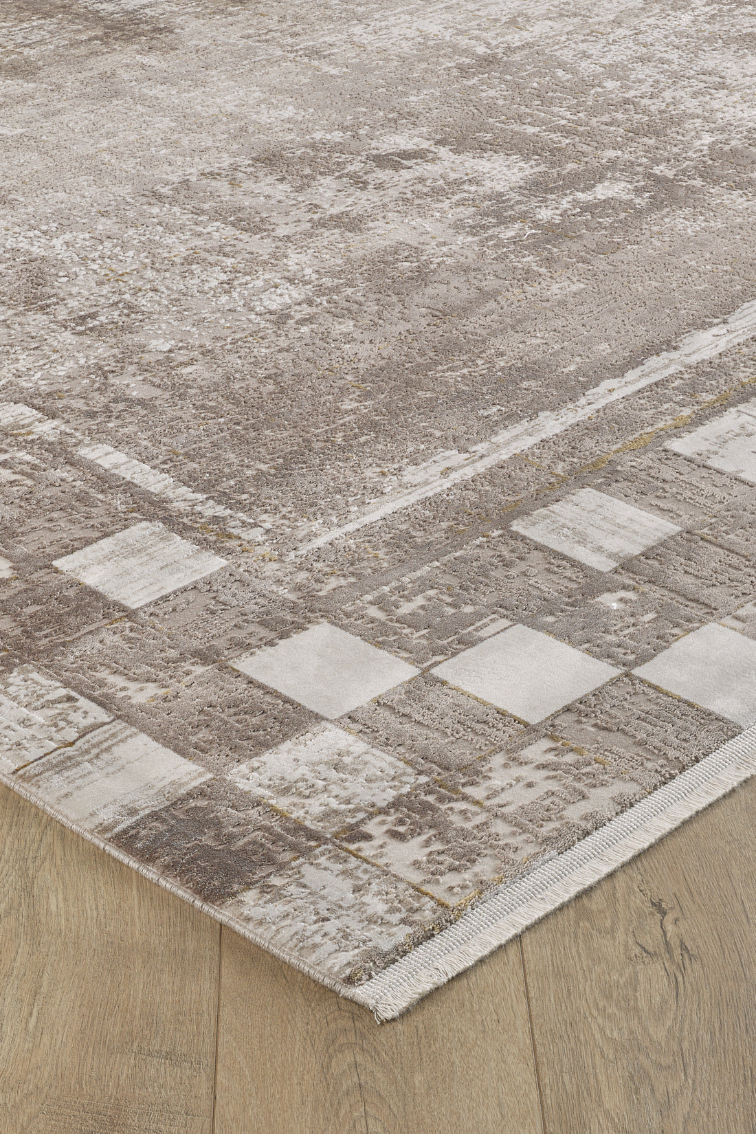 A close-up of the Geometric Latte Premium Rug - M420G, a machine-made beige and brown rug with a subtle geometric pattern and a border of light and dark squares, adds minimalist style to any light wood floor.