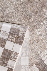 A close-up of the Geometric Latte Premium Rug - M420G shows a folded corner revealing its square geometric underside and textured beige and light brown surface, ideal for a modern, minimalist décor.