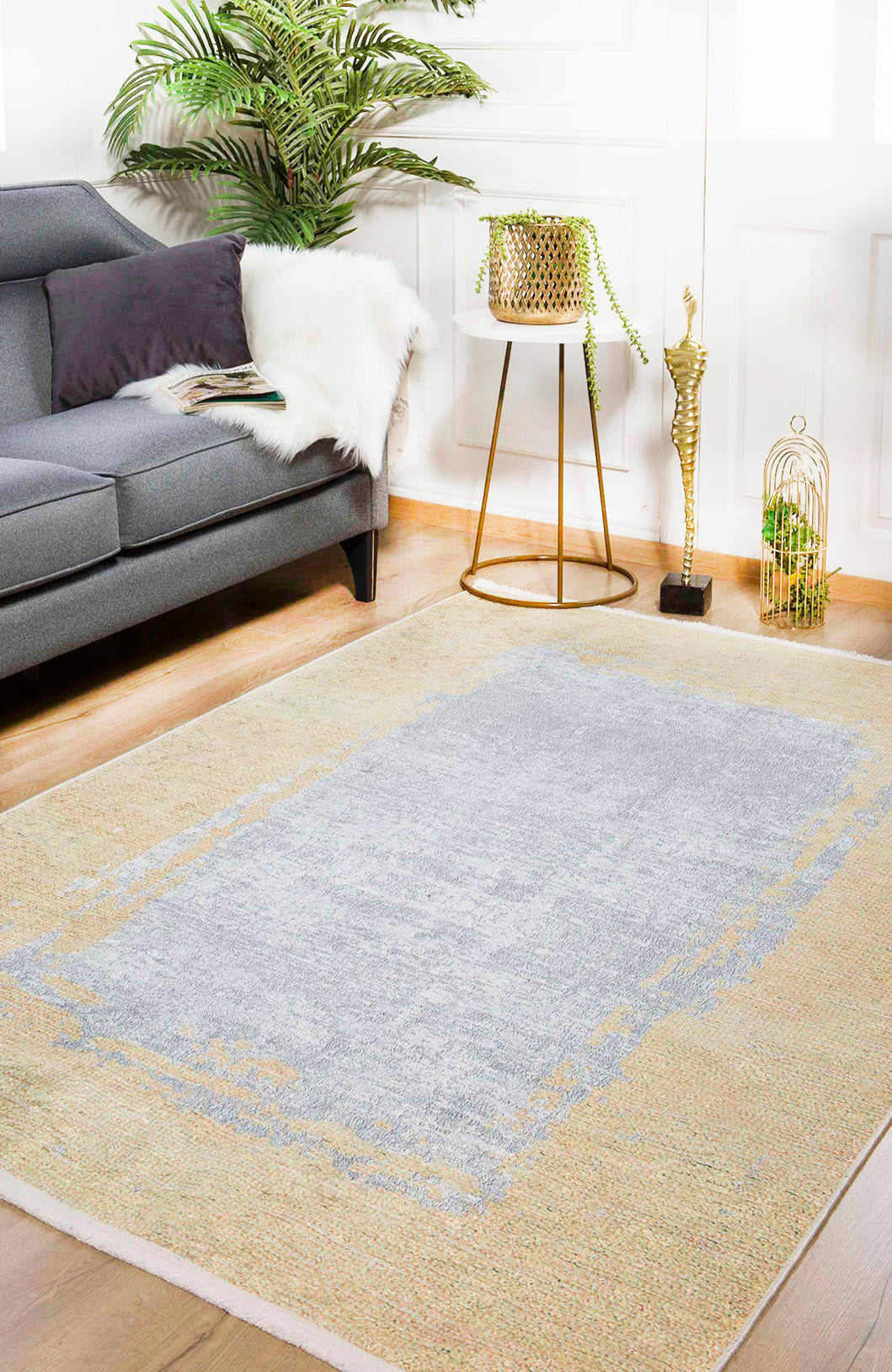 A modern living room with a gray sofa, fur throw, potted plant on a gold tripod stand, a gold sculpture, and the Geometric Trellis - Washable Rug - JR931 (Custom Size) with gray center—perfect for high-traffic spaces.
