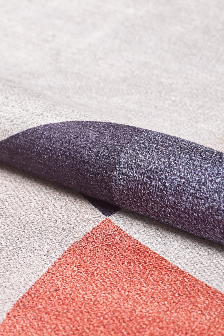A close-up of the Geometric Zen Modern Washable Rug - MDJ002, featuring textured geometric shapes in purple, red, cream, and beige tones, folded to show its thickness and weave—perfect for allergy-sensitive spaces.