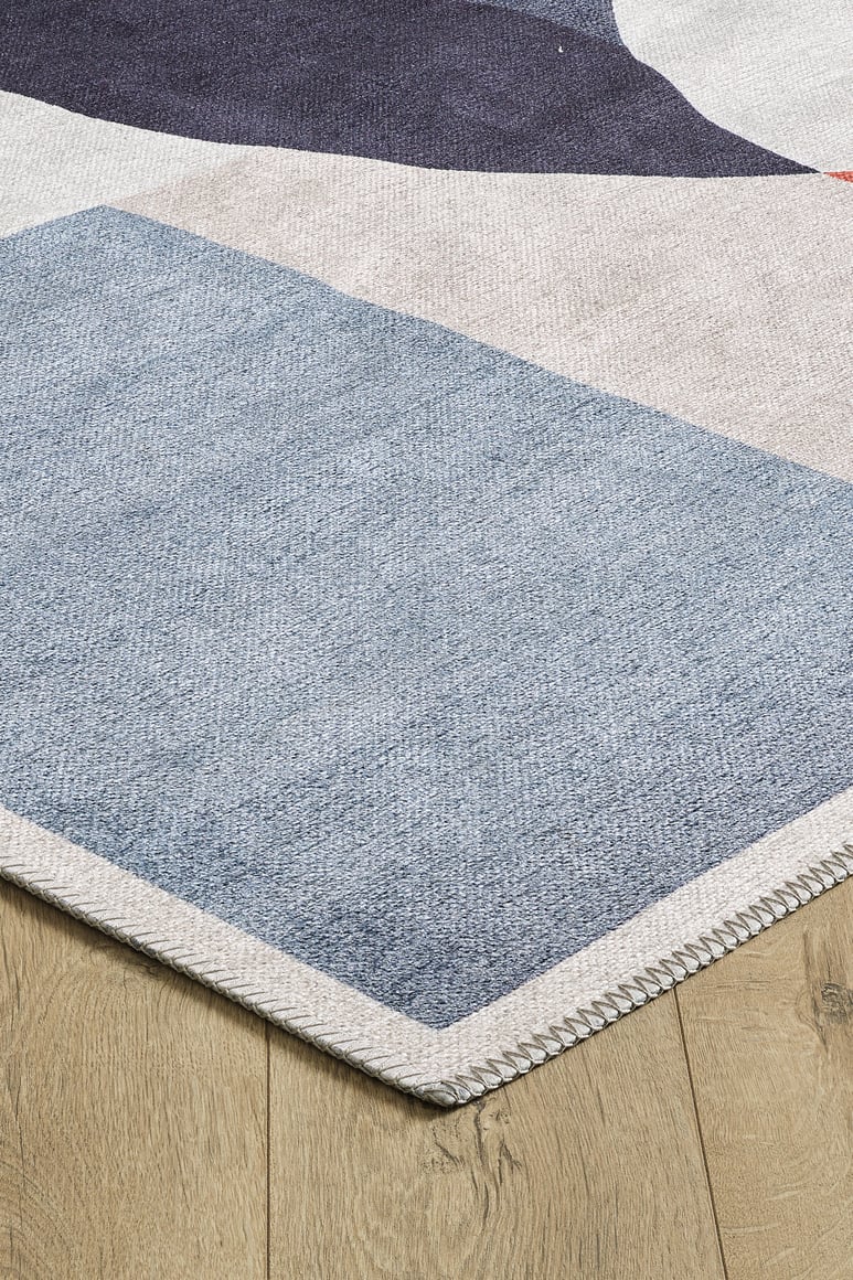 A close-up of the Geometric Zen Modern Washable Rug - MDJ002 (Custom Size) shows blue, white, and purple geometric patterns with a stitched edge. Ideal for high-traffic areas, it's placed on a light wood floor.