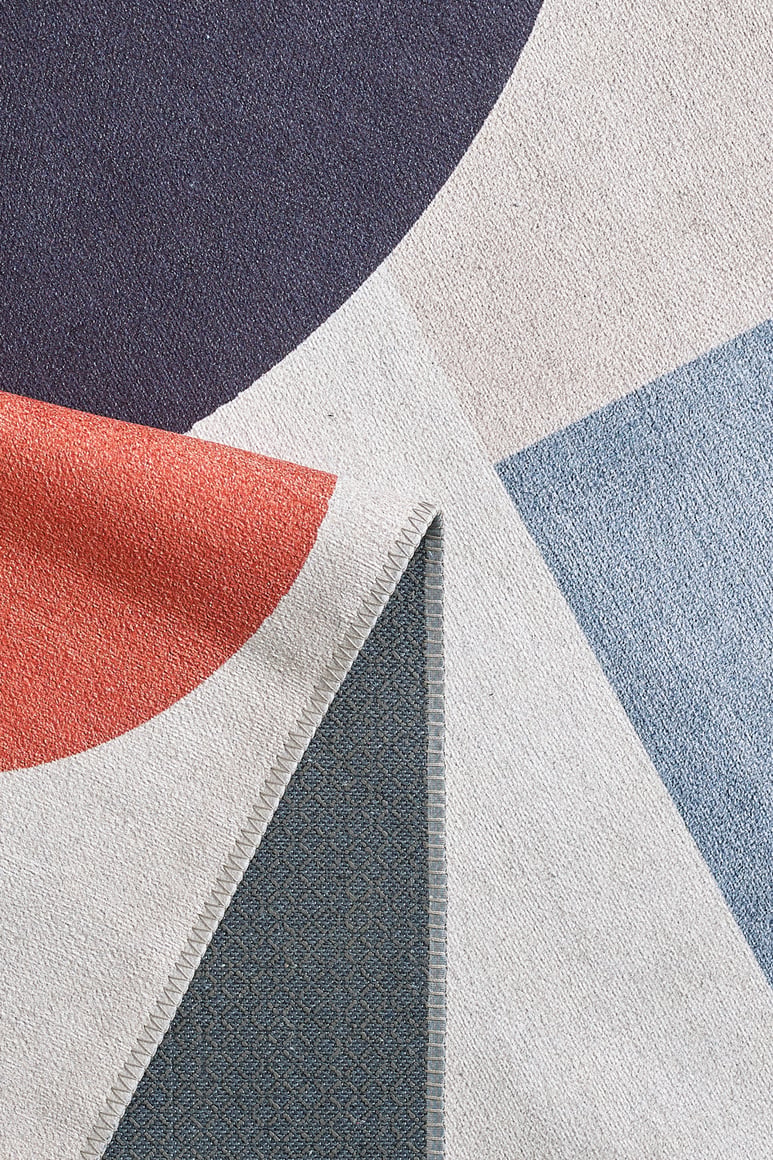 A close-up of the Geometric Zen Modern Washable Rug - MDJ002 (Custom Size) in navy, red, light blue, and gray on cream. The folded corner shows the underside, highlighting its durability for high-traffic areas.