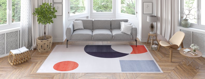 Modern living room with a gray sofa, beige lounge chair, round wooden coffee table, potted plant, and large windows. The space features light wood floors and a Geometric Zen Modern Washable Rug - MDJ002 (Custom Size) for easy care and style.