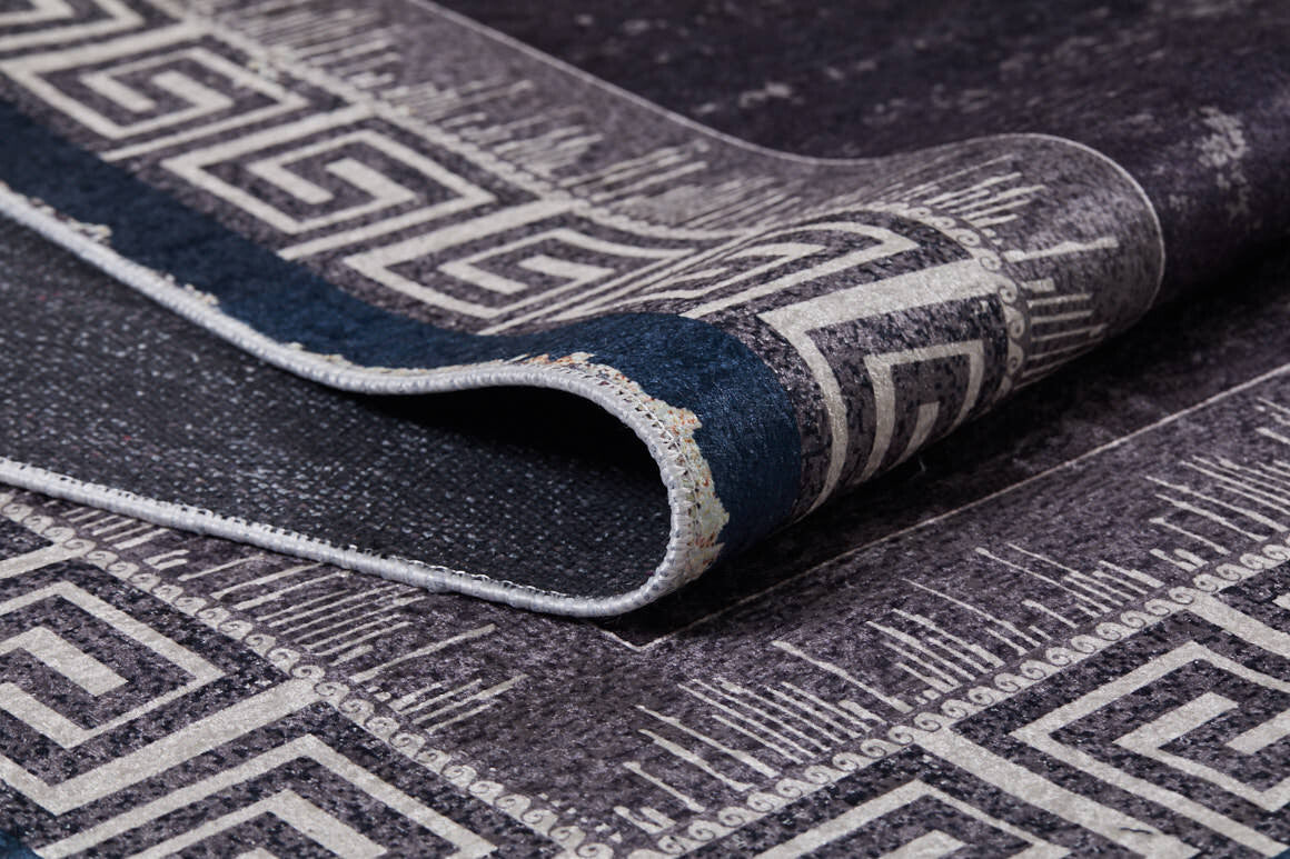 A close-up of the Geometric and Chic - Washable Rug - JR1273 (Custom Size), featuring a dark tone and white Greek key border pattern, partially folded to show front and back textures—perfect for high-traffic spaces.