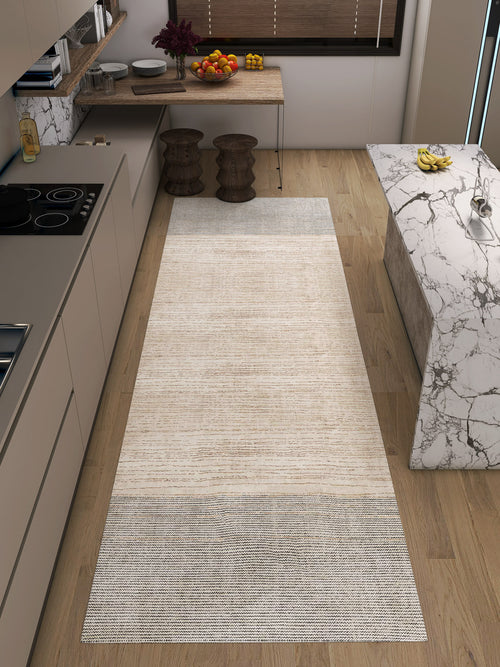 Load image 1 in gallery view. A modern kitchen with light wood floors features the Gilded Charm - Washable Rug - JRN26 (Custom Size), a flat weave beige and gray runner perfect for high-traffic areas, paired with marble counters, a stove, bar stools, fruit bowls, and brown blinds.