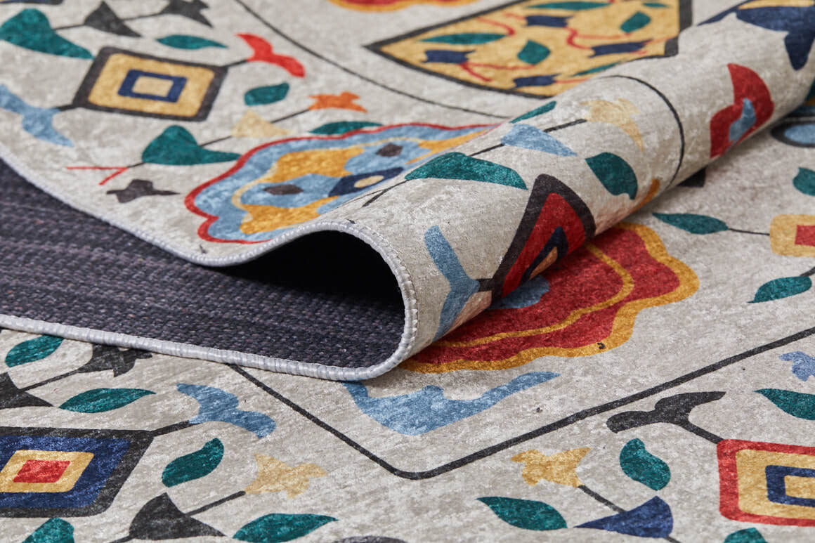 A close-up of the Global Gathering - Washable Rug - JR608 (Custom Size) displays its vibrant geometric and floral design with a lifted corner, revealing a textured, dark underside—ideal for high-traffic areas.