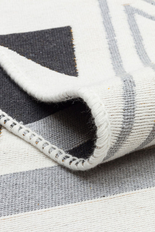 Load image 1 in gallery view. Close-up of the Golden Fog - Washable Double-Sided Kilims - AR18 rug with a folded corner, showing its geometric black, gray, and white pattern, visible stitched edge, and durable recycled cotton texture.