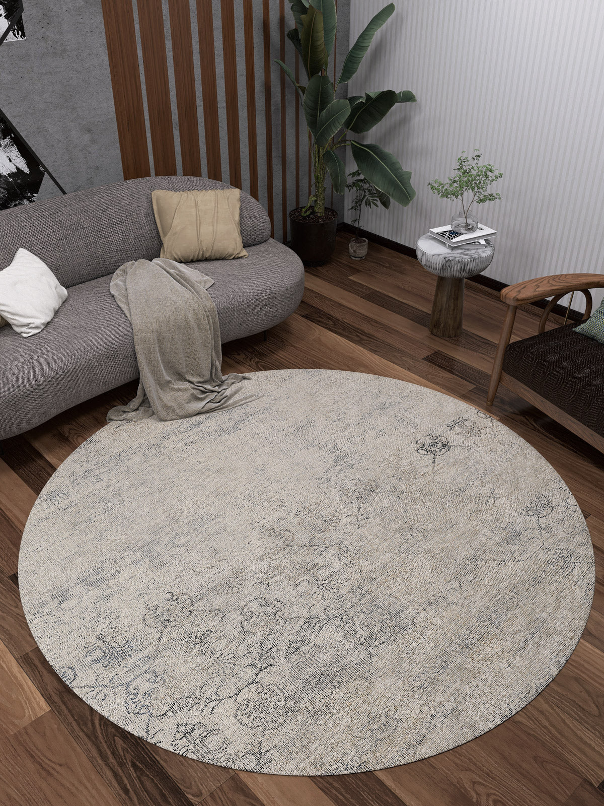 A modern living room features the Graceful Tapestry - Washable Rug - JR1975 on dark wood floors, a curved gray sofa with cushions and a throw, a wooden chair, a side table with a plant, and a tall houseplant in the corner.