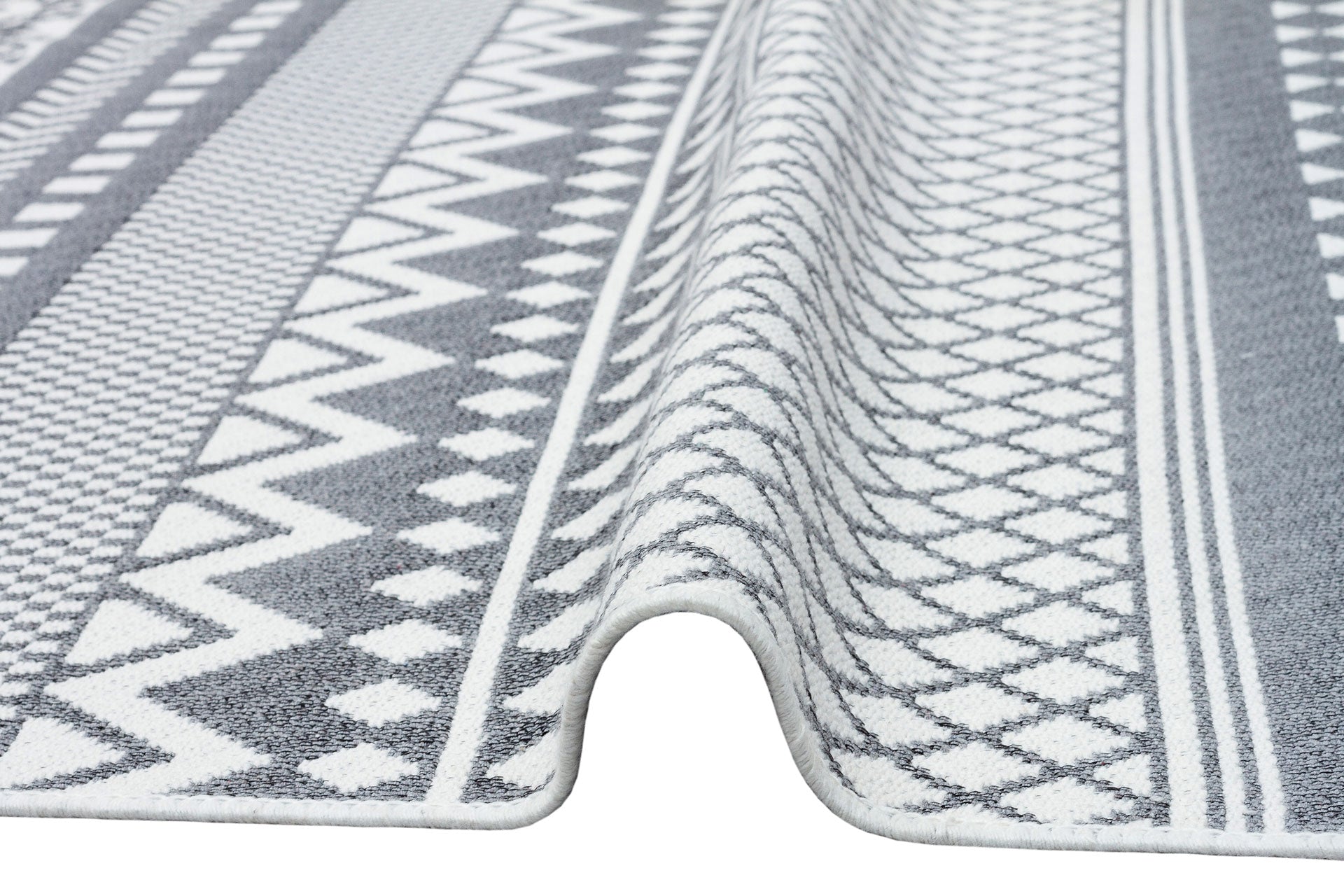 A close-up of the Grey Drift - Washable Double-Sided Kilims - AR07, featuring geometric designs in grey and white with a raised wave-like fold in the center.