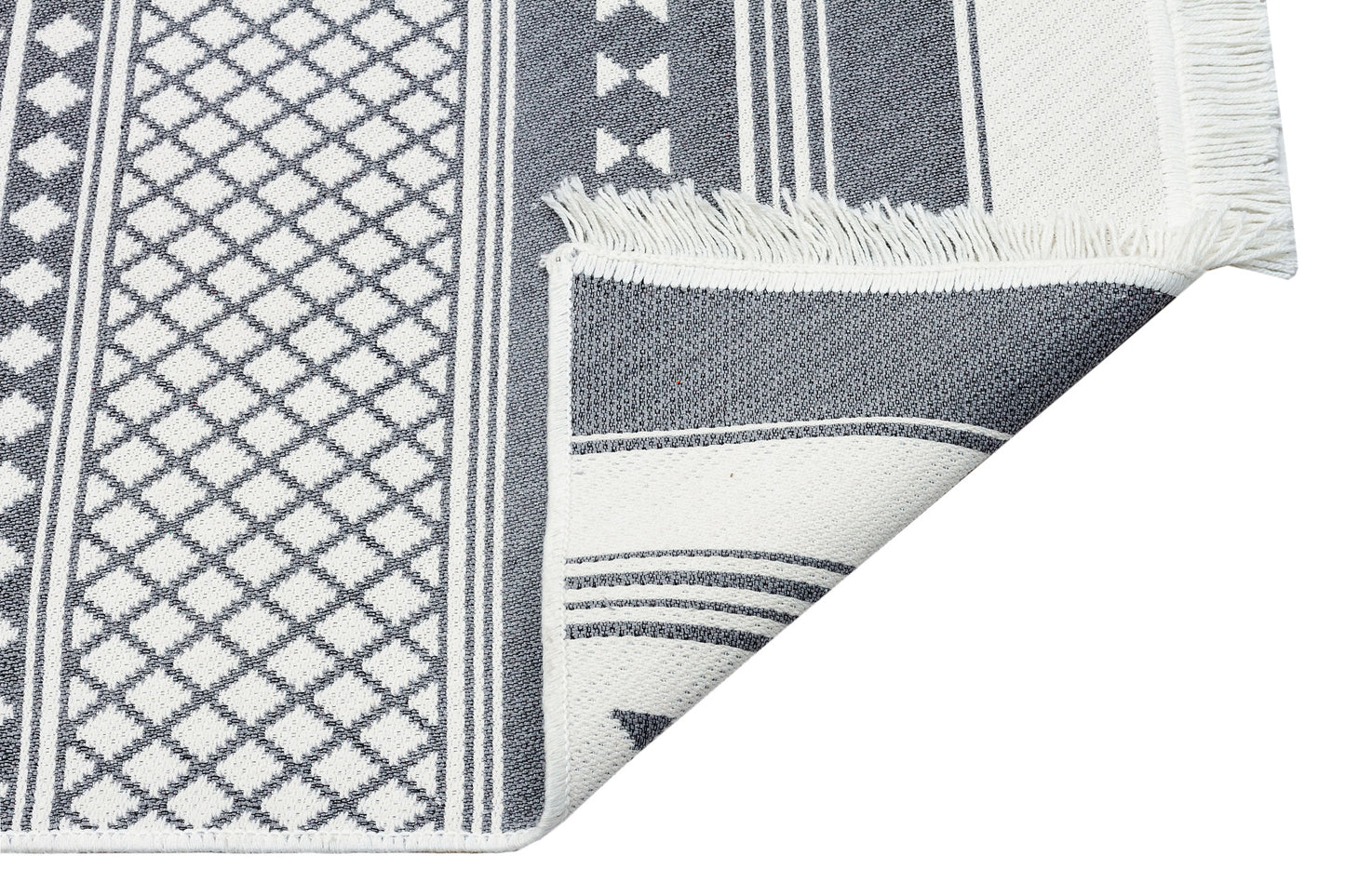 A close-up of the Grey Drift - Washable Reversible Kilims - AR07 rug features black and white geometric patterns, fringed edges, and a folded corner displaying the tribal design on both sides.