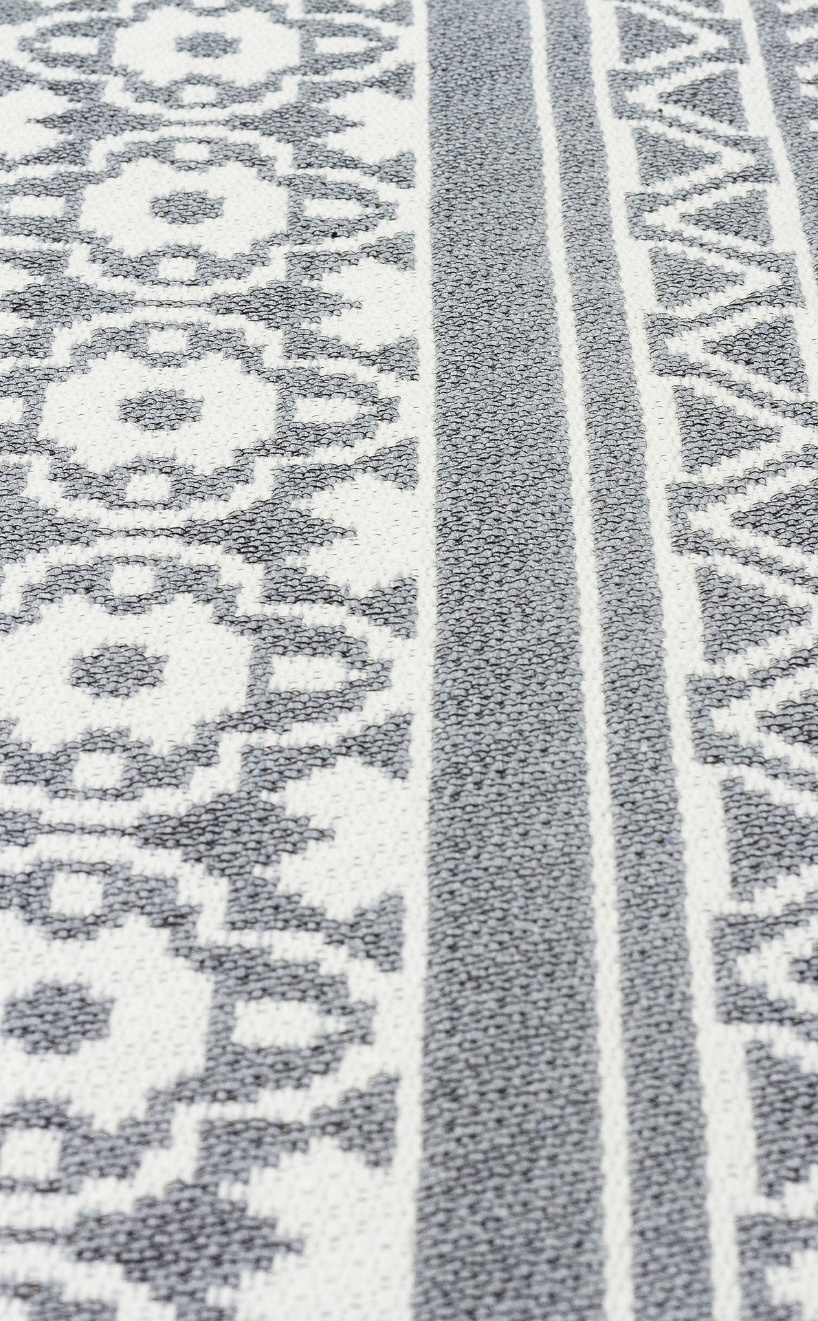 A close-up of the Grey Drift - Washable Reversible Kilims - AR07 rug, showcasing gray and white geometric and floral patterns with alternating stripes, inspired by tribal motifs.